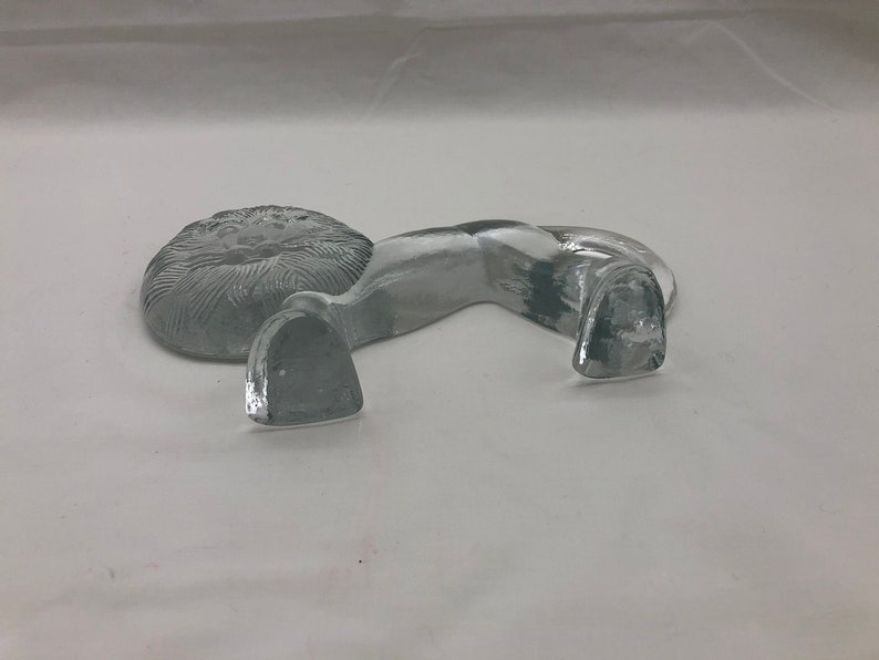 K&ouml;nnte beinhalten: Eine durchsichtige Glasfigur eines L&ouml;wen mit detaillierter M&auml;hne. Der L&ouml;we liegt mit dem Kopf zur Seite gedreht.