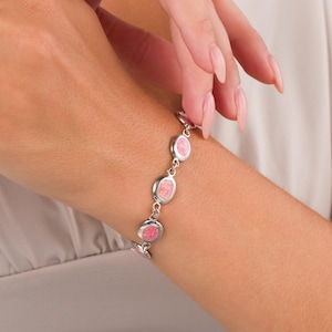 May include: A silver bracelet with oval pink opal stones. The bracelet is made up of linked ovals, each with a pink opal. The bracelet is worn on a wrist.