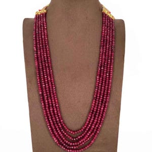 May include: A multi-strand necklace with small, faceted, ruby-red beads. The necklace is displayed on a brown mannequin bust. The clasp and connecting elements appear to be gold-colored.