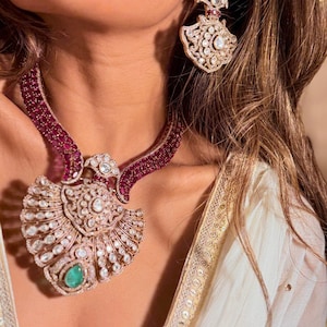 May include: A luxurious necklace and earring set. The necklace features a large, ornate pendant with a central emerald and surrounding diamonds. The necklace and earrings have a gold tone with ruby accents. The earrings match the necklace design.
