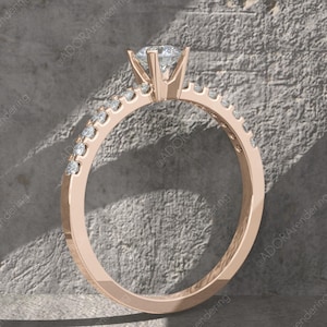 May include: Rose gold engagement ring with a large, clear center stone and smaller stones set along the band. The ring is set against a textured gray background, with shadows adding depth. A classic and elegant design.