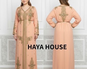 May include: A peach-colored, long-sleeved dress with intricate gold embroidery and a matching gold belt. The dress features a V-neckline and is embellished with small, sparkling details. The text "HAYA HOUSE" is displayed in black.