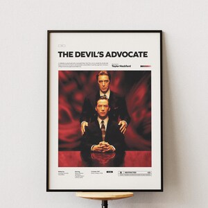 May include: Framed movie poster for "The Devil's Advocate" featuring two men in suits against a red backdrop. The title is at the top, with the director's name below. The poster is in a black frame.