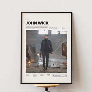 May include: Framed movie poster for "John Wick" with a man in a black suit holding a gun. The poster includes the movie title and director's name. The background depicts an industrial setting with the word "RESTRICTED".