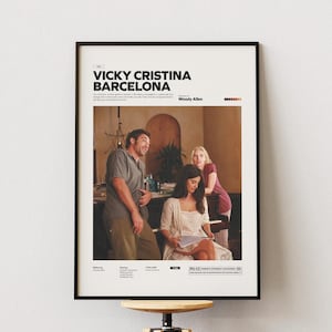 Könnte beinhalten: Gerahmtes Filmplakat für "Vicky Cristina Barcelona" mit schwarzem Rahmen. Das Plakat zeigt eine Szene aus dem Film mit drei Personen. Titel und Credits sind in weißer Schrift oben. Das Plakat wird an einer weißen Wand gezeigt.
