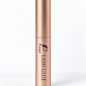 May include: A cylindrical rose gold lash glue tube with a matching cap. The label features the text iPamper LASH GLUE in black, accompanied by a small purple and gold logo graphic. The bottom of the tube is clearly marked with the text NET 5ML.