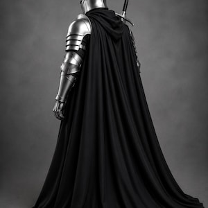 May include: A suit of polished silver metal armor featuring a rounded helmet with a central spike, articulated shoulder and arm plates, and a long, flowing black hooded cloak. A longsword with a black grip is strapped across the back.
