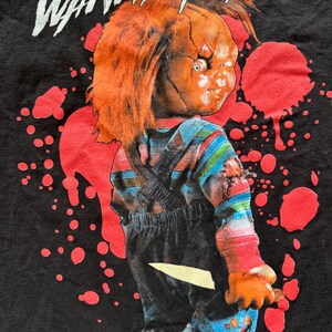 black Mad Engine Chucky "Wanna Play?" T-Shirt featuring a graphic of the Chucky doll holding a knife with red blood splatters and WANNA PLAY