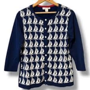 May include: Navy blue cardigan with white sailboat pattern. The long-sleeve sweater has a round neckline and button-down front. The garment is hanging on a wooden hanger.