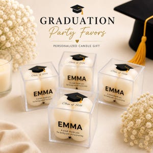 May include: Four square clear plastic boxes containing cream-colored bubble candles. Each candle features a black graduation cap icon, the text "Class of 2026", the name "EMMA", and the phrase "A small thank you for being part of my journey".