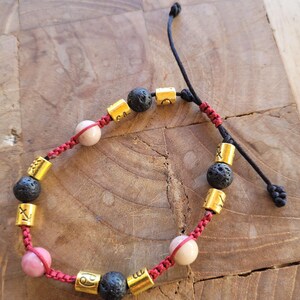 Peut inclure: Bracelet réglable avec un cordon rouge, des perles en métal doré avec des symboles du zodiaque, des perles de lave noires et des perles de pierres précieuses roses. Fermeture coulissante.