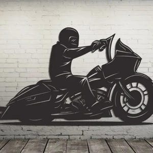 Può includere: Arte da parete in metallo nero raffigurante una motocicletta con un pilota. La silhouette mostra una persona con un casco su una moto dettagliata. L'opera d'arte è montata su un muro di mattoni bianchi.