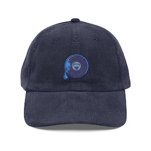 Puede incluir: Gorra de béisbol de pana azul marino con un diseño bordado de un disco con efecto de goteo. El disco tiene bordadas las letras "DJO". La gorra tiene una visera curva y una correa ajustable.