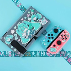 May include: A clear gray Nintendo Switch case and Joy-Con controllers featuring a teal-haired anime character design. The controllers are blue and pink with matching character accents. Decorative tape with Japanese text is also visible.