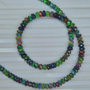 May include: Strands of faceted opal beads in a variety of colors, including green, blue, red, and black. The beads are strung together, creating a necklace or bracelet. The opals have a shimmering, iridescent quality.