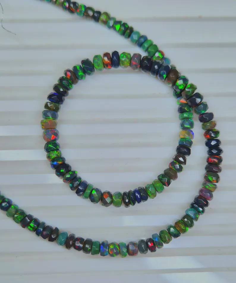 May include: Strands of faceted opal beads in a variety of colors, including green, blue, red, and black. The beads are strung together, creating a necklace or bracelet. The opals have a shimmering, iridescent quality.