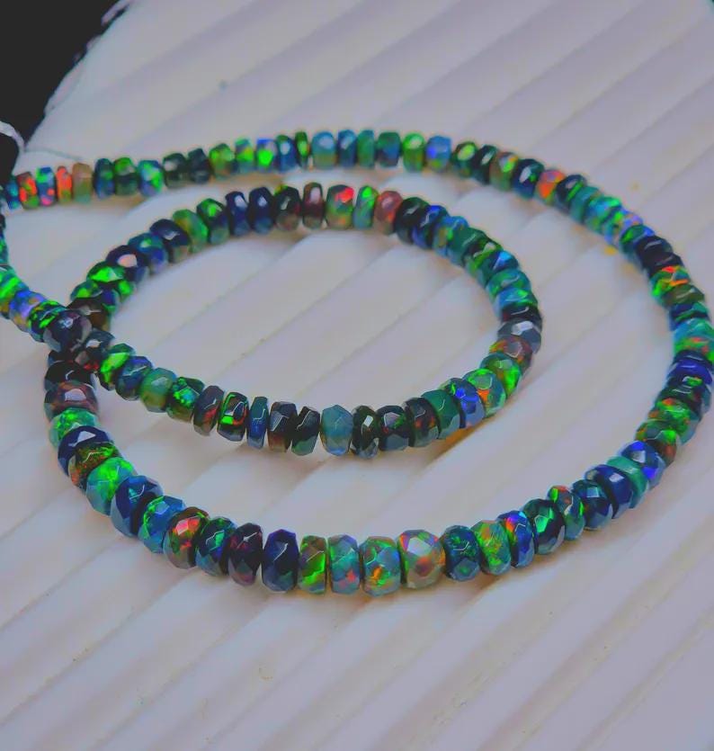 May include: Two strands of faceted opal beads in a variety of colors, including green, blue, and red. The beads are strung together to form a necklace or bracelet. The opals have a sparkling, iridescent quality.
