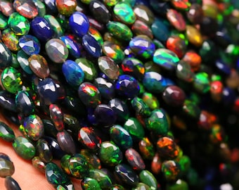 May include: Strands of faceted black opal beads. The beads display a variety of colors, including green, blue, red, and yellow, with a polished, reflective surface. The beads are oval-shaped and strung together.