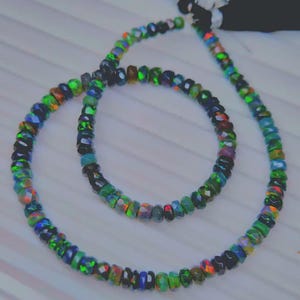 May include: Two strands of faceted opal beads in a variety of colors, including green, blue, orange, and black. The beads are strung together to form a necklace and bracelet set. The beads have a polished finish and reflect light.
