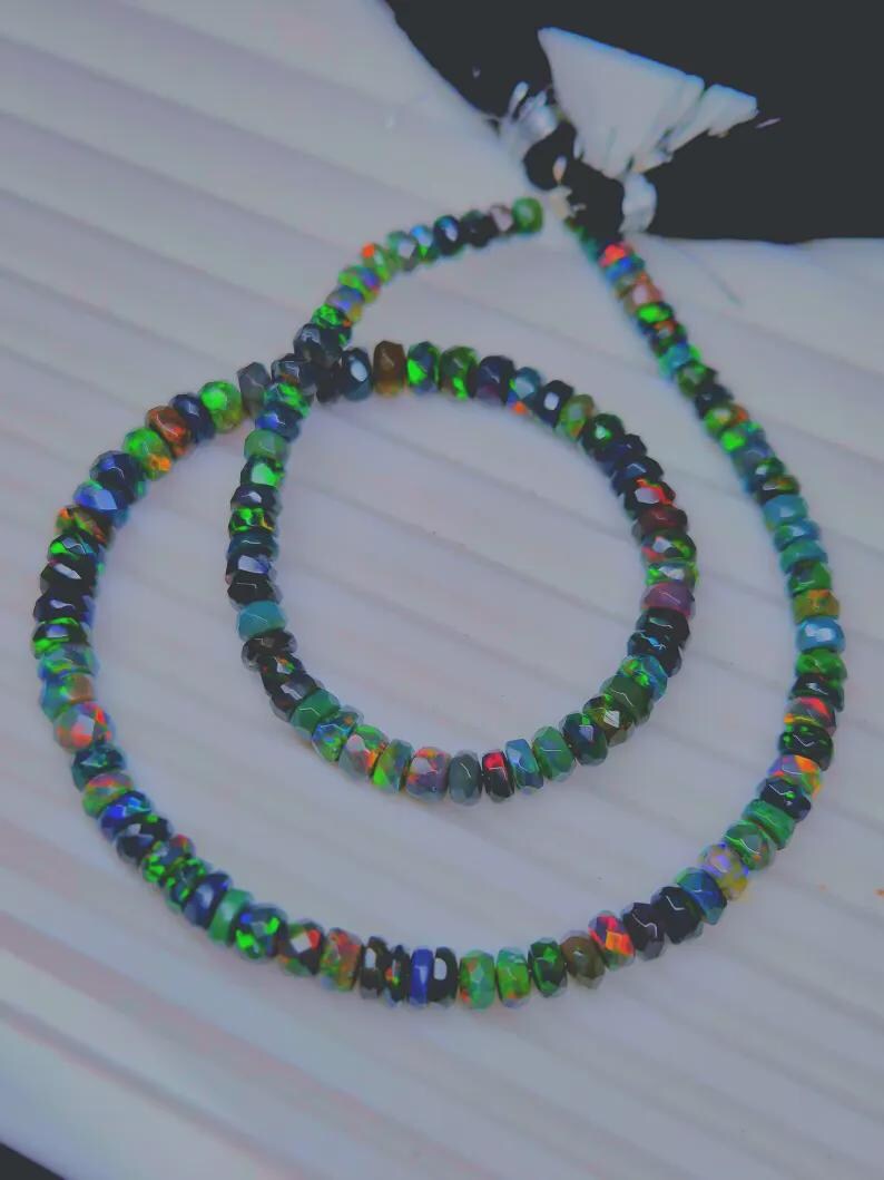 May include: Two strands of faceted opal beads in a variety of colors, including green, blue, orange, and black. The beads are strung together to form a necklace and bracelet set. The beads have a polished finish and reflect light.