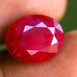 Peut inclure: Une pierre précieuse rubis de taille ovale d'un rouge profond, dotée d'une surface à facettes qui reflète la lumière. La pierre présente des caractéristiques de clarté interne et une finition polie, mettant en valeur une forme classique.