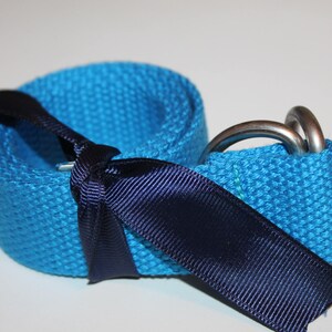 May include: A blue canvas belt with a silver buckle and a black ribbon tied around it.