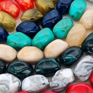 May include: A selection of polished gemstone beads in a variety of colours and shapes. The beads are in shades of red, gold, blue, teal, cream, and black with marbled and translucent effects. Suitable for jewellery making.