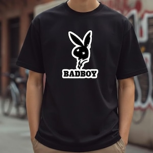 May include: Black t-shirt featuring a white graphic of a bunny head with a cross-shaped eye and the word "BADBOY" in a white, bold font. The shirt is short-sleeved and appears to be made of cotton.