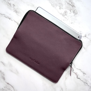 May include: A dark plum-colored textured leather tablet sleeve with a black zipper closure. The word myFolio is embossed on the front surface. A silver-colored tablet is partially inserted into the sleeve, revealing its top edge and camera lens.