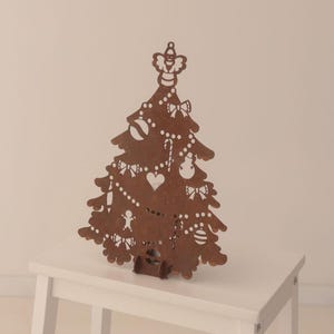 May include: A brown wooden Christmas tree decoration with cut-out ornaments, including bows, hearts, and candy canes. The tree is decorated with a star on top and stands on a small white table.