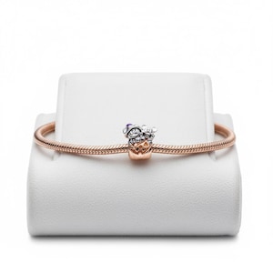 May include: A rose gold bracelet with a charm featuring two cartoon characters in Halloween costumes. The charm has silver and gold tones with purple and orange accents. The bracelet is displayed on a white stand.