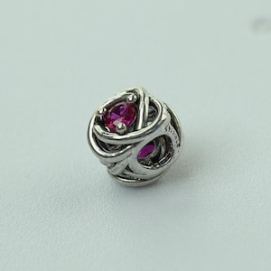 May include: A spherical silver charm bead featuring an intricate, swirling openwork design. The metal surface is accented with two vibrant, oval-cut pink stones set within the loops. The side of the bead is engraved with the text S925 ALE.