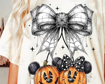 May include: Cream-colored t-shirt featuring a Halloween-themed graphic. The design includes a large, detailed bow with spiderwebs, and two smiling jack-o'-lanterns with Mickey Mouse ears. Black stars are scattered around the design.