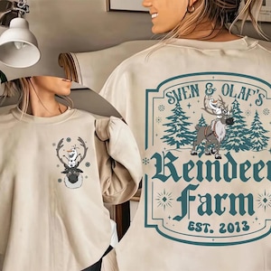 Pode incluir: Camisola bege com um desenho de Sven e Olaf de Frozen. A frente tem uma pequena imagem de Sven com Olaf em seus chifres. A parte de tr&aacute;s tem um design maior com o texto "Sven & Olaf's Reindeer Farm EST. 2013".