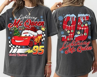 Può includere: Una maglietta grigia con un design natalizio con Saetta McQueen di Cars. La parte anteriore della maglietta mostra McQueen con un cappello da Babbo Natale che guida un'auto da corsa rossa con il numero 95. La parte posteriore della maglietta mostra il numero 95 con luci di Natale e fiocchi di neve. Il testo "Lightning Mc Queen" e "Merry Christmas" è anche sulla maglietta.