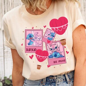 Puede incluir: Una camiseta beige claro con un dise&ntilde;o de dibujos animados rosa y azul con Stitch y Angel de la pel&iacute;cula de Disney Lilo & Stitch. El dise&ntilde;o incluye corazones, estrellas y globos aerost&aacute;ticos. El texto "XOXO" y "Be Mine" tambi&eacute;n est&aacute;n incluidos en el dise&ntilde;o.