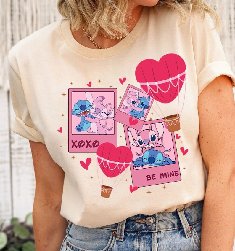 Puede incluir: Una camiseta beige claro con un dise&ntilde;o de dibujos animados rosa y azul con Stitch y Angel de la pel&iacute;cula de Disney Lilo & Stitch. El dise&ntilde;o incluye corazones, estrellas y globos aerost&aacute;ticos. El texto "XOXO" y "Be Mine" tambi&eacute;n est&aacute;n incluidos en el dise&ntilde;o.