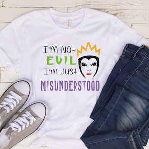 May include: White t-shirt with a graphic of the Evil Queen from Snow White. The graphic includes the text "I'm not evil, I'm just misunderstood" and a crown. The shirt is paired with blue jeans and gray sneakers.