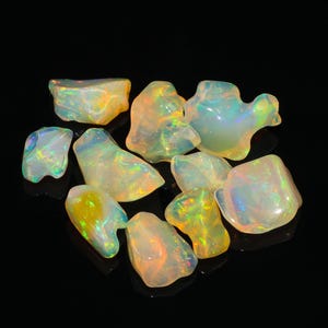 May include: A collection of raw, translucent opals with irregular shapes and smooth surfaces. These gemstones exhibit a play of colour, featuring flashes of yellow, orange, green, and blue light against a milky, semi-transparent base.
