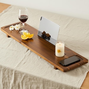 Puede incluir: Una bandeja de bañera de madera marrón oscuro con una copa de vino, rodajas de naranja, un espejo pequeño, una vela encendida y un teléfono inteligente. La bandeja tiene forma rectangular con bordes elevados.