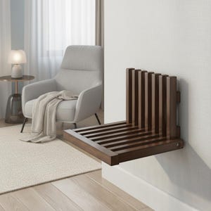 Könnte beinhalten: Ein an der Wand montierter, dunkelbrauner Klappsitz aus Holz. Der Sitz hat ein Latten-Design und eine vertikale Rückenlehne mit gleichmäßig verteilten Holzlatten. Er ist an einer weißen Wand montiert, mit einem hellen Teppich und einem Sessel im Hintergrund.
