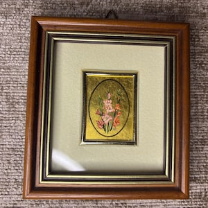 May include: A framed artwork with a gold background and a floral design in pink and red. The artwork is set within a wooden frame with a gold inner border and a cream-coloured mount.
