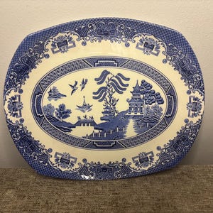 May include: Oval blue and white ceramic serving platter with a Willow pattern design. The platter features a central scene of a pagoda, trees, and birds, surrounded by a decorative border. The platter measures approximately 36 cm long.