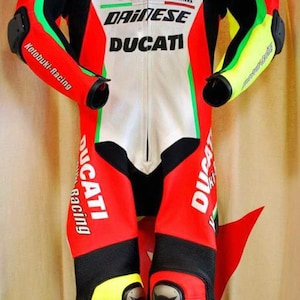 May include: A red, white, black, and green motorcycle racing suit with the logos "Kotobuki-Racing", "de LIGHT", "DAINESE", and "DUCATI". The suit has yellow accents on the shoulders, elbows, and knees.
