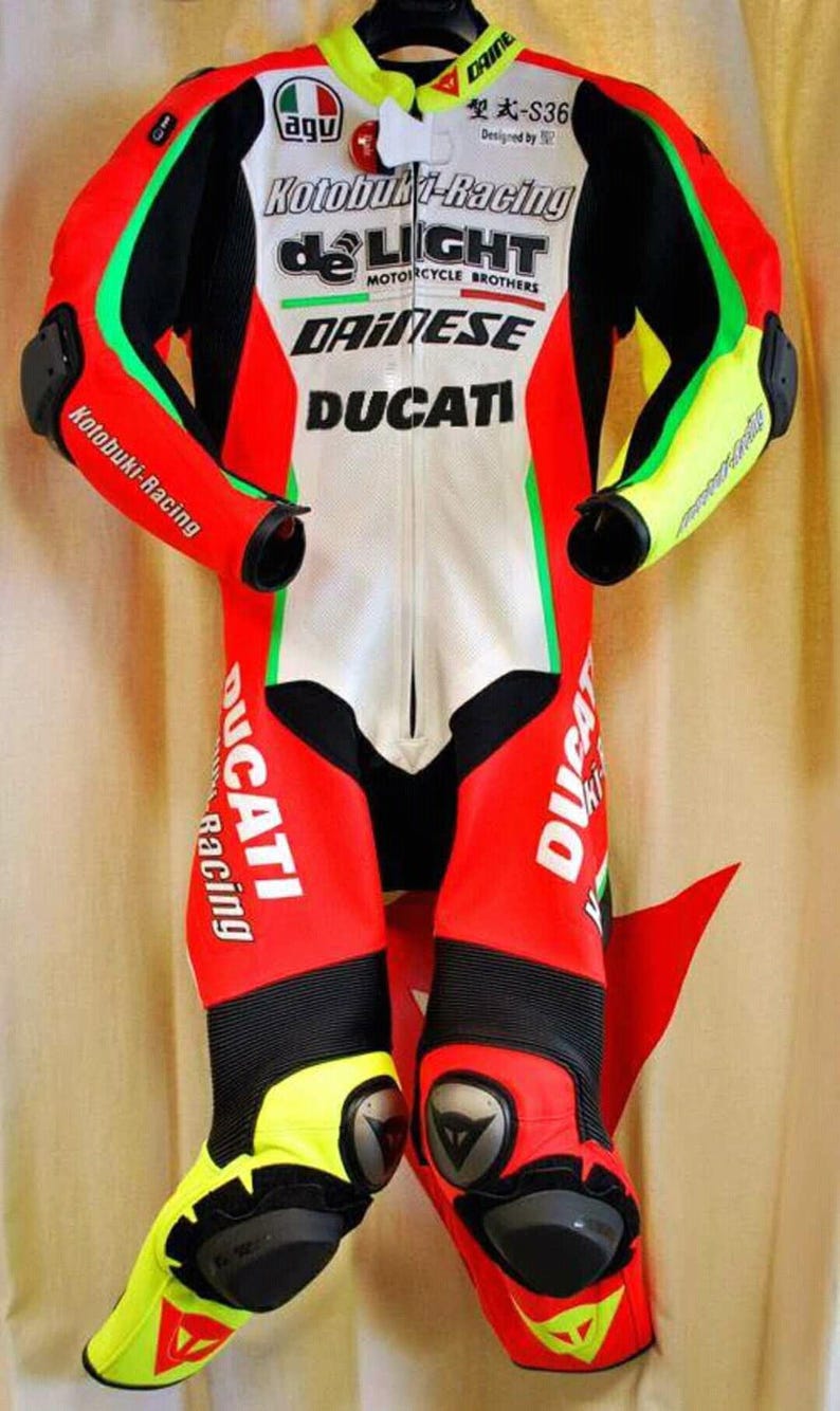 May include: A red, white, black, and green motorcycle racing suit with the logos "Kotobuki-Racing", "de LIGHT", "DAINESE", and "DUCATI". The suit has yellow accents on the shoulders, elbows, and knees.