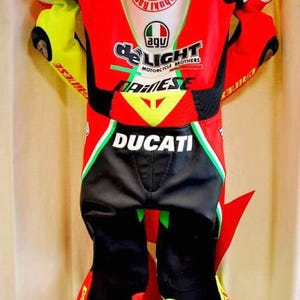 May include: A red, black, and yellow Ducati motorcycle racing suit. The suit features the Ducati logo, along with other sponsor logos and text. The suit has a white panel on the back with Japanese text and a circular logo.