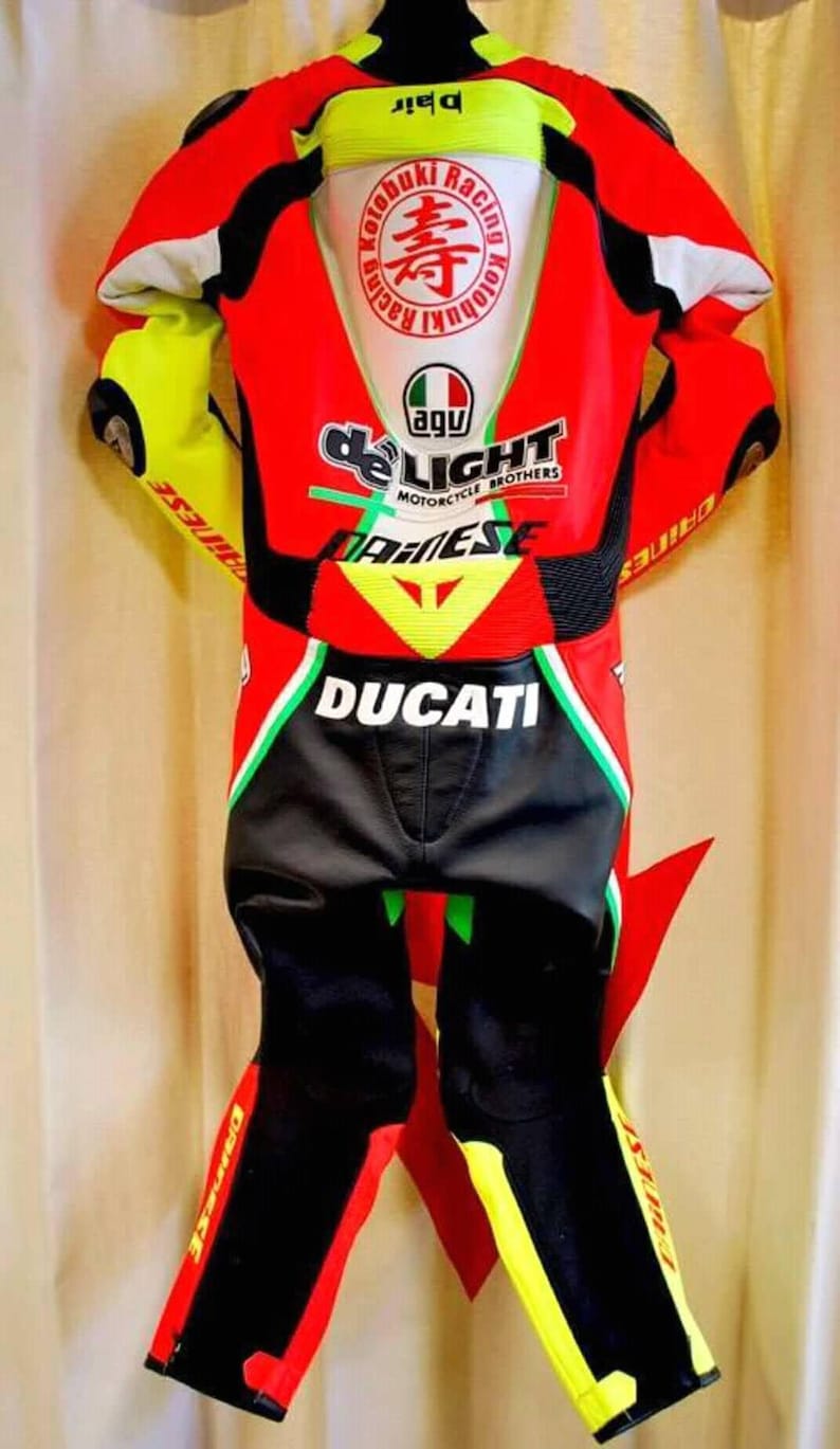 May include: A red, black, and yellow Ducati motorcycle racing suit. The suit features the Ducati logo, along with other sponsor logos and text. The suit has a white panel on the back with Japanese text and a circular logo.
