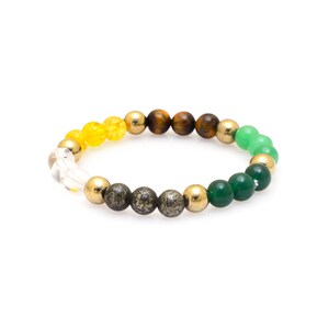 Könnte beinhalten: Ein Armband mit bunten Perlen. Das Armband enthält klare, gelbe, goldene, braune, grüne und dunkelgraue Perlen. Die Perlen sind auf einem Gummiband aufgereiht und bilden ein Stretch-Armband.