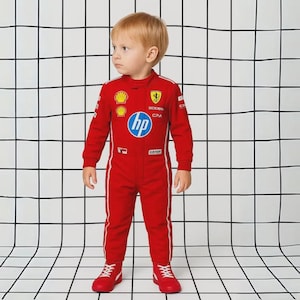 May include: A red racing jumpsuit with white stripes and logos, including "hp" and "Ferrari", worn with matching red shoes. The jumpsuit has a high collar and long sleeves. The child is standing in front of a black and white grid.