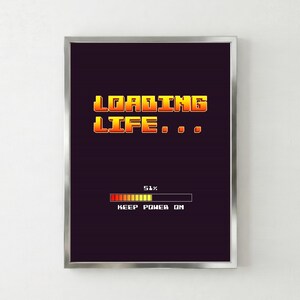 Könnte beinhalten: Ein gerahmter Druck mit einer Retro-Videospiel-Ästhetik. Die Worte "LOADING LIFE..." sind in orangefarbener und gelber Pixel-Schriftart gehalten. Darunter zeigt ein Fortschrittsbalken 51 % Fertigstellung an, mit dem Text "KEEP POWER ON". Der Hintergrund ist dunkelviolett.